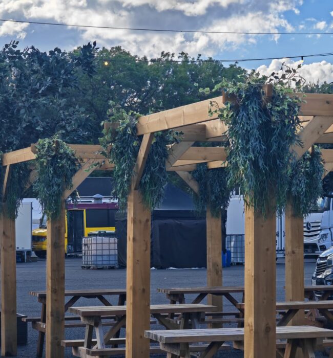 Artificial trailing foliage for hire, hung from wooden pergola posts, with artificial trees behind at Download Festival