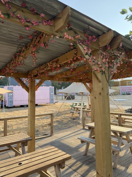 Artificial pink cherry blossom garlands for hire, wound along the wooden pergola beams over festival picnic benches
