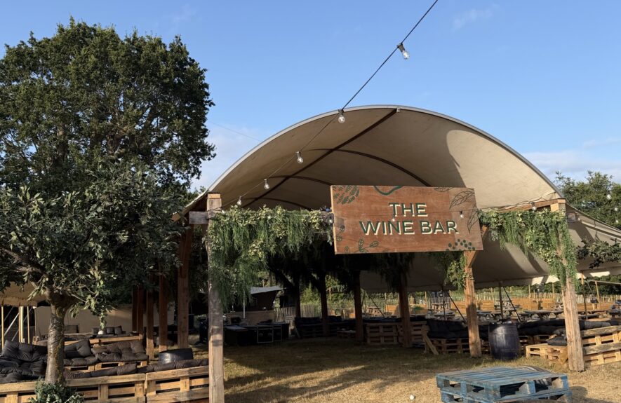 Artificial tree for hire, in a wooden planter beside a foliage-garlanded 'The Wine Bar' sign at a festival