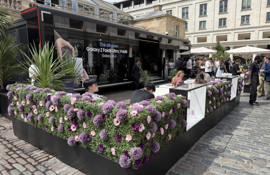 Artificial flowered hedge panels for hire, placed either side of a lit display window with Samsung phones, Covent Garden